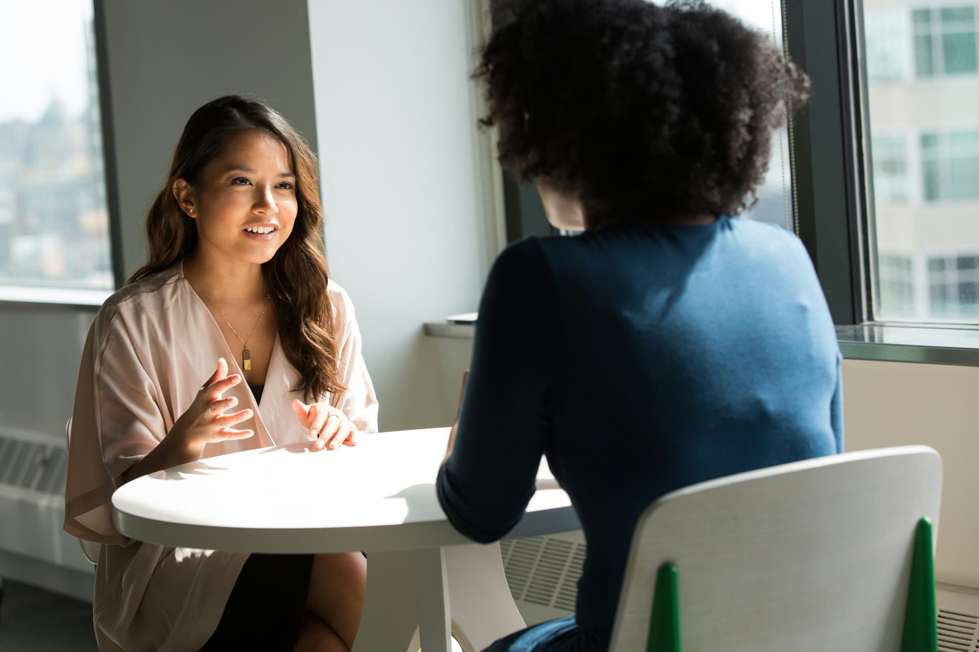 Two people engaged in a conversation at a table near a window.
