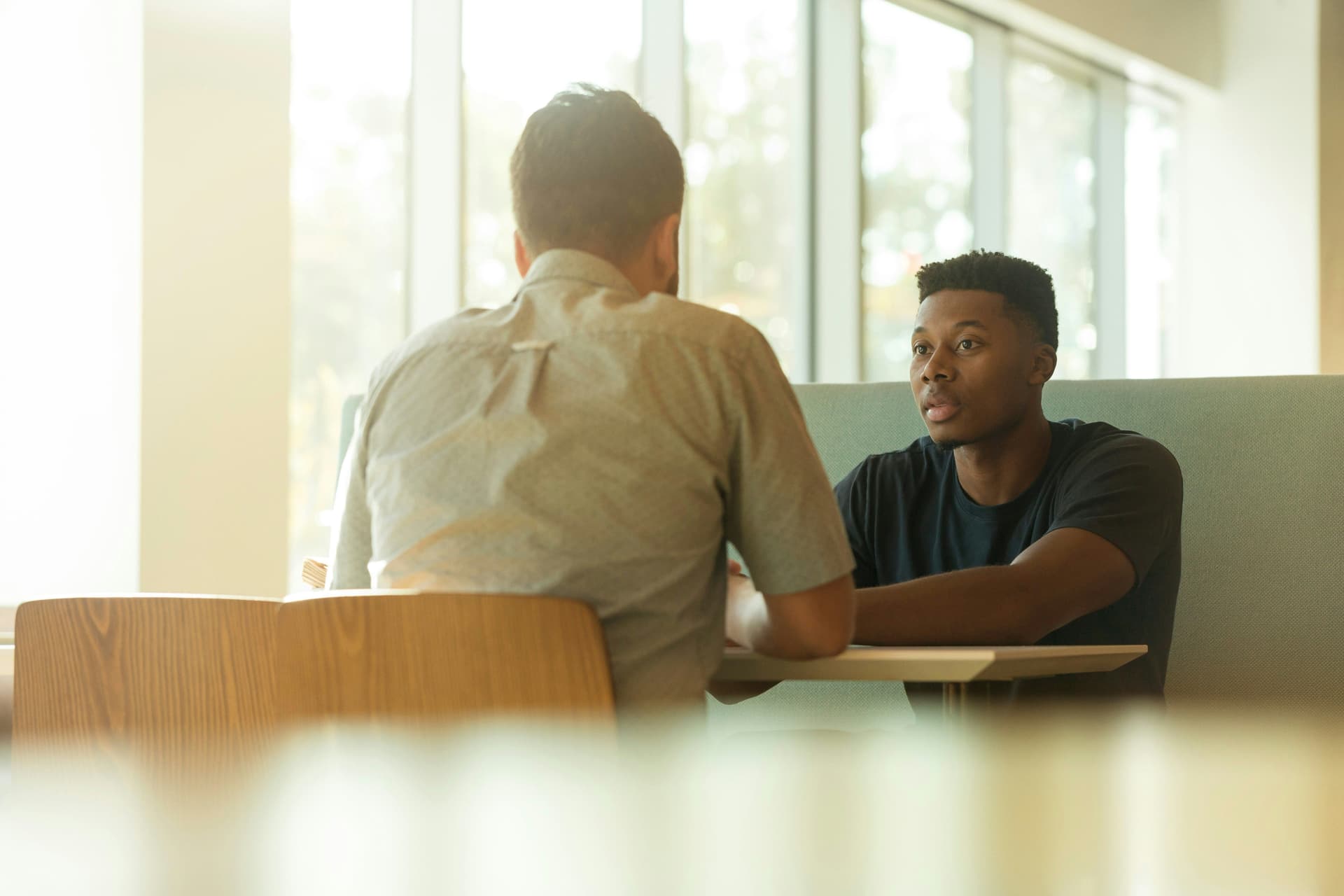 Two individuals seated at a table having a conversation indoors.